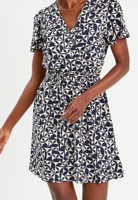 Robes à manches courtes avec un décolleté en V profond, présentant un motif géométrique bleu marine et crème et une taille élastique pour une silhouette ajustée.
