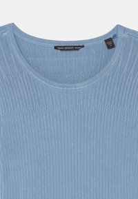 Svetle modrý žebrovaný pletený svetr s kulatým výstřihem a jemnou texturou. Štítek s názvem značky "GUESS" na černém štítku.