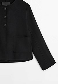 Veste en laine noire avec trois boutons, col rond, manches longues et une grande poche carrée sur le côté avant gauche.