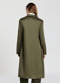 Cappotto lungo verde oliva con una texture liscia, revers a punta, maniche lunghe e un design minimalista. Presenta un taglio dritto sul retro.