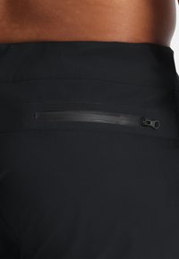 Pantaloni sportivi neri con una tasca zip nascosta sul retro. Il materiale è liscio con una finitura opaca, che enfatizza un design elegante.