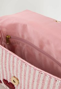 Gyöngyös kézitáska rózsaszín szatén béléssel, cipzáras zsebbel, fehér és rózsaszín gyöngyökkel díszítve, valamint egy díszítő szív motívummal.