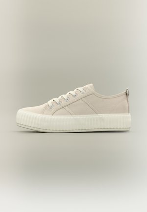 Baskets basses en toile beige avec semelle épaisse en caoutchouc blanc et lacets, vues de profil sur un fond neutre.