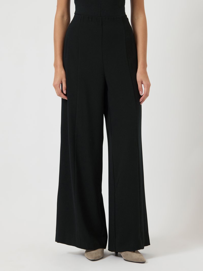 Μαύρο παντελόνι με φαρδιά μπατζάκια από μαλακό ύφασμα, με ψηλή μέση και πλισέ μπροστά. Η λεία υφή και οι καθαρές γραμμές τονίζουν το σχέδιο.