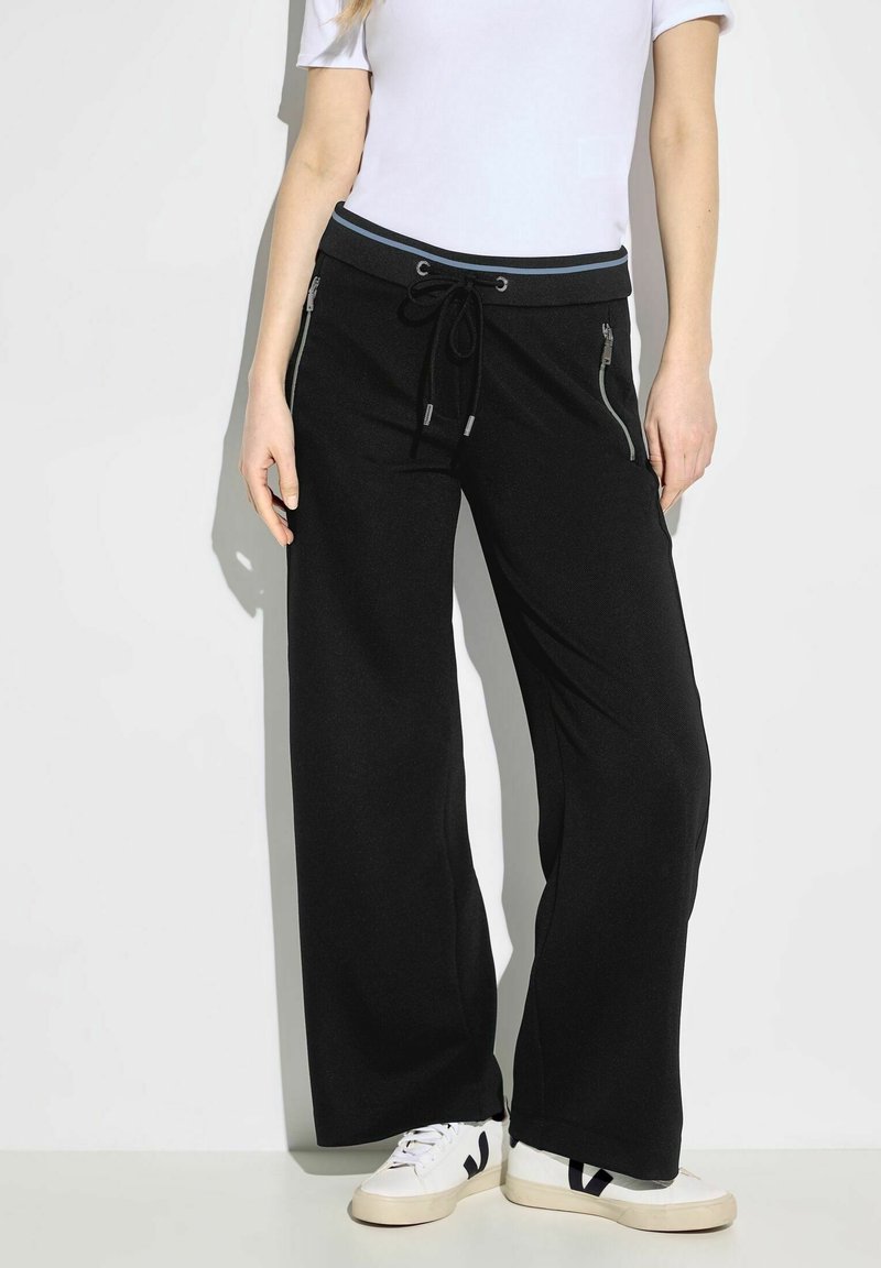 Svarta vida byxor i mjukt tyg, med dragsko i midjan och sidogylf. Matchas med vita sneakers.