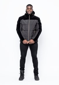 Svart vadderad jacka med en mjuk, texturerad överdel, dragkedja och huva. Bärs med svarta byxor och stövlar, med en avslappnad passform.