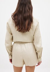 Beige linen shirt and shorts set with an elastic waistband, featuring long sleeves and subtle button accents on the cuffs.