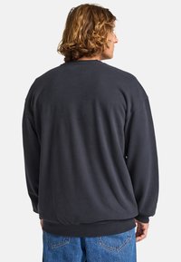 Sudadera negra de corte relajado, con puños y dobladillo acanalados, textura suave y costuras de hombro caídas, combinada con jeans azul claro.