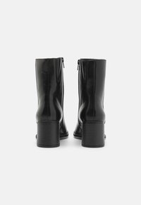 Black leather ankle boots with a smooth finish, featuring a side zipper and a ribbed block heel. The design is sleek and form-fitting.