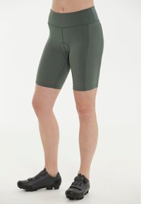 Gröna cykelshorts i stretchigt material, med en åtsittande design och en midjehöjd som är mellan hög och låg. Matchat med robusta svarta cykelskor.