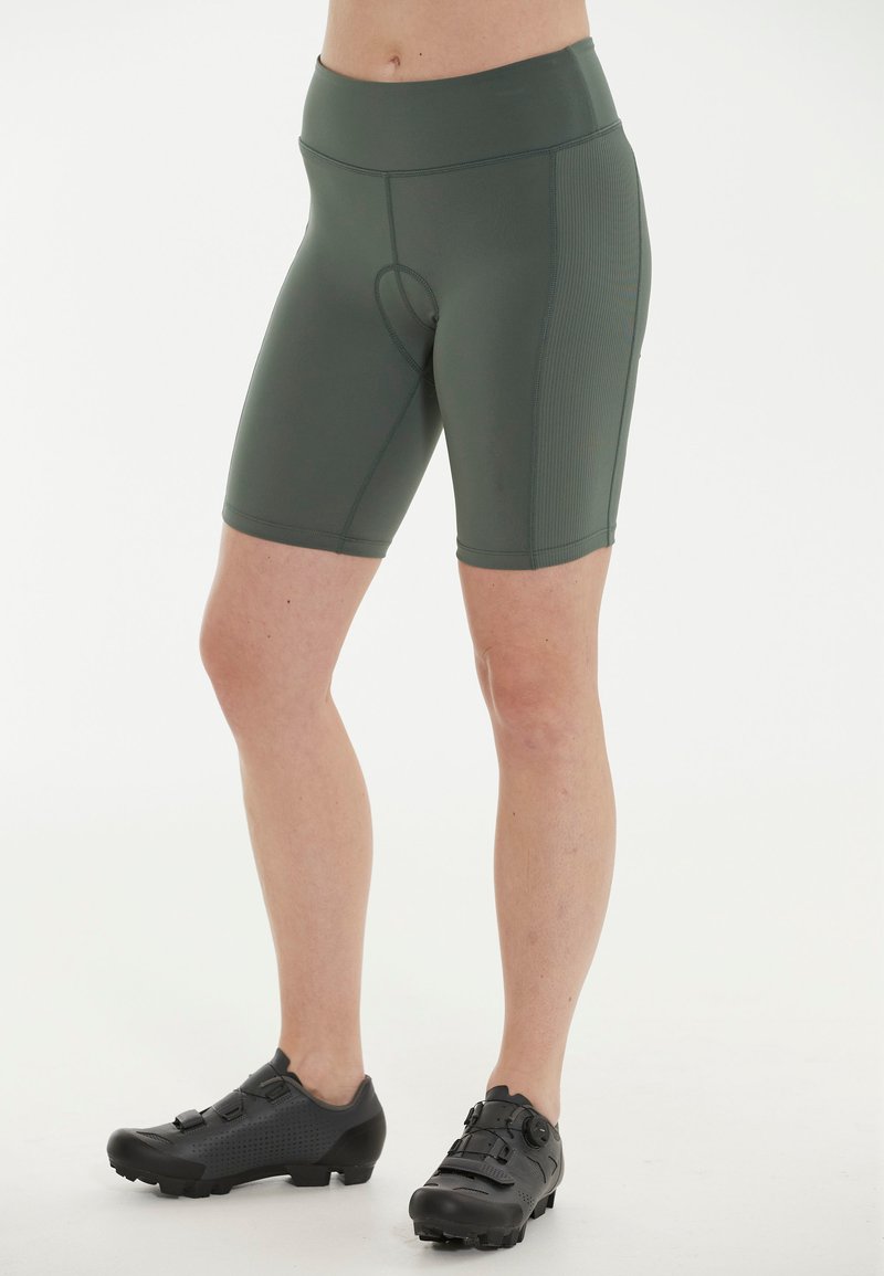 Gröna cykelshorts i stretchigt material, med en åtsittande design och en midjehöjd som är mellan hög och låg. Matchat med robusta svarta cykelskor.