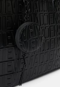 Sort håndtaske lavet af præget læder med brandnavnet. Den inkluderer en rund lynlåset møntpung, der er fastgjort med en kæde.