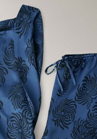 Ensemble de vêtements en tissu bleu avec motifs floraux noirs, comprenant un haut avec col et un pantalon à taille coulissante.