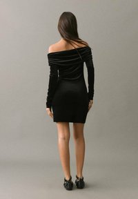 Rochie neagră din catifea, cu umerii la vedere, mâneci lungi și o siluetă ajustată, având o textură moale și detalii minime.