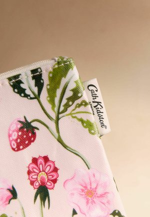 Lähikuva kankaasta, jossa vihreitä lehtiä, punainen mansikka, vaaleanpunaisia kukkia ja valkoinen etiketti, jossa lukee Cath Kidston.