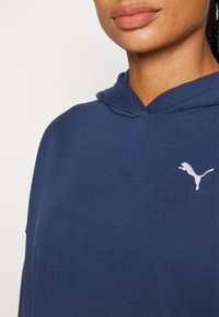 Navy modra kapuca z v-izrezom, izdelana iz mehke tkanine; na levem prsnem predelu je bel logotip pume.
