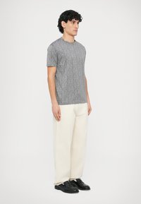 Szara koszulka z geometrycznym wzorem, zestawiona z beżowymi spodniami o szerokich nogawkach i czarnymi eleganckimi butami. Prosty krój i krótkie rękawy.