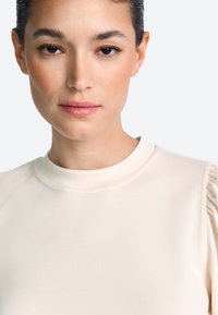 Top de culoare crem cu decolteu rotund și mâneci ușor bufante, având o textură fină și un croi ajustat.