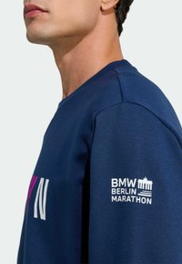 Navy sweatshirt with ribbed collar and cuffs. Features large pink and white "BERLIN" text and a white logo for the BMW Berlin Marathon on the sleeve.