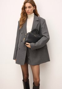 Czarna skórzana torebka o usztywnionym kształcie, ze złotymi akcentami i górną rączką; noszona z szarym, w paski oversize'owym żakietem i szortami.