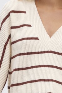 Pull crème à côtes avec un décolleté en V profond, présentant des rayures horizontales marron. Texture douce avec une coupe décontractée et des épaules tombantes.