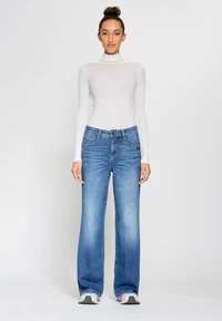 Lightweight white ribbed turtleneck, paired with blue wide-leg jeans featuring five pockets and subtle stitching detail, complemented by sneakers.