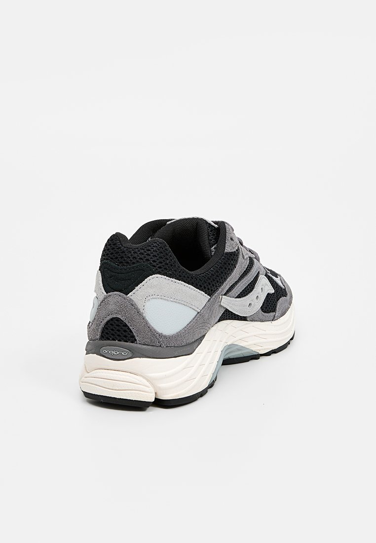 Baskets de sport noires, grises et blanches avec tige en mesh et suédé, semelle épaisse et rembourrée, et détail de marque sur le côté, vues de l'angle arrière.