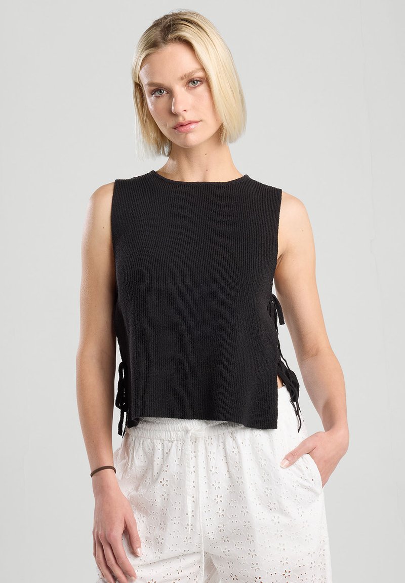 Black sleeveless knit top with ribbed texture, featuring side ties for adjustment. Paired with white drawstring shorts with eyelet pattern.