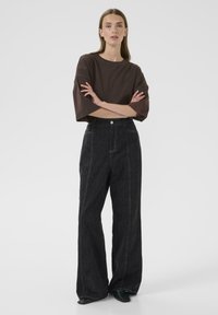Barna, oversized póló és magas derekú sötét farmer széles szárú nadrág kontrasztöltésekkel és gombos elejével. Elegáns fekete bokacsizma.