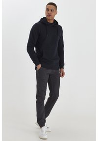 Sudadera con capucha de color navy con un bolsillo frontal, combinada con pantalones gris oscuro y zapatillas blancas. La tela es suave con un corte casual.
