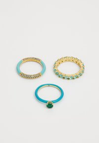 Tre anelli: uno in oro con gemme blu, uno in smalto turchese con una pietra verde e uno in oro con piccoli sassolini teal in un design circolare.