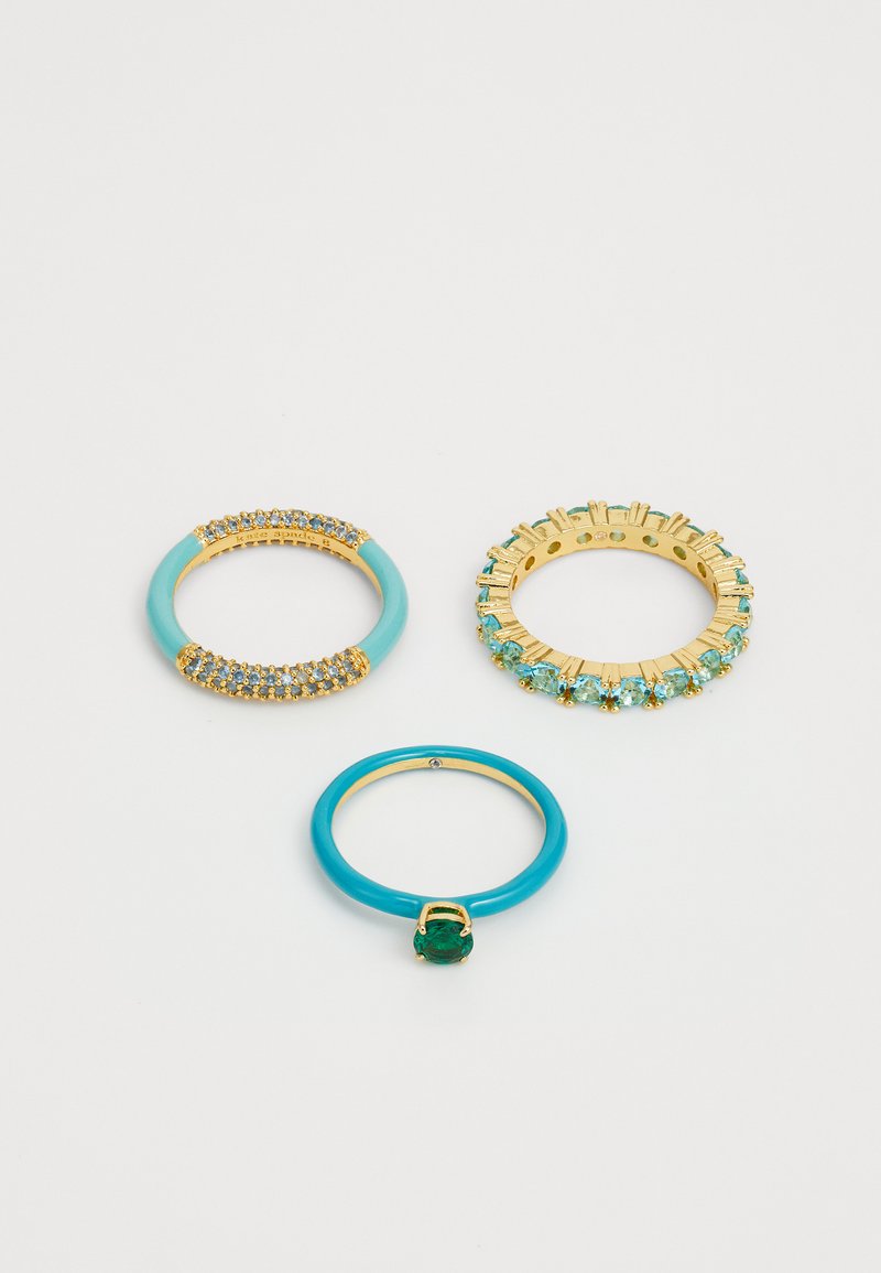 Tre anelli: uno in oro con gemme blu, uno in smalto turchese con una pietra verde e uno in oro con piccoli sassolini teal in un design circolare.