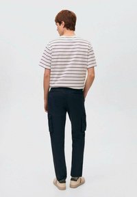 Črtasta majica s kratkimi rokavi v beli in mornarsko modri barvi, v kombinaciji z mornarsko modrimi cargo hlačami, ki imajo stranskežepe, ter svetlobezhnimisupergami.