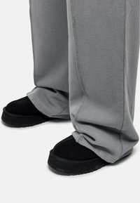 Szare dresowe spodnie o luźnym kroju, w połączeniu z czarnymi butami na slip-on z grubą podeszwą i miękką zamszową teksturą.