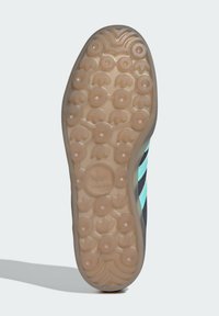 Suola di scarpa nera e blu con motivo di trazione circolare, con accentuazioni a strisce turchesi e un logo rotondo al centro. Gomma beige testurizzata.