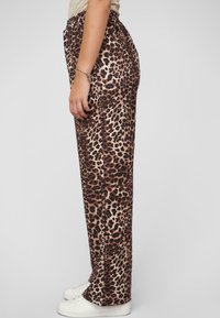Luipaardprint broek met een elastische tailleband, tapse vorm en een gladde textuur. Draagt met witte sneakers.