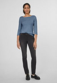 Blauer Pullover mit langen Ärmeln und Rundhalsausschnitt, kombiniert mit schwarzen Slim-Fit-Jeans und schwarzen Schuhen mit dicker Sohle. Glatter Stoff.