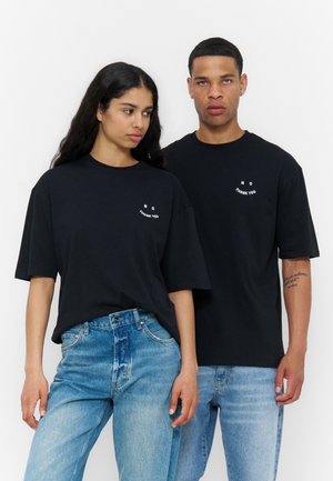 To personer iført sorte oversize t-shirts med teksten "NO THANK YOU", kombineret med lyseblå jeans, står side om side.