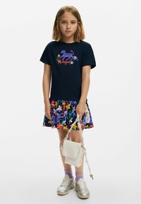 Tricou bleumarin cu un design vibrant floral și cu tigri, asortat cu o fustă colorată cu imprimeu. Tenisi argintii și o geantă mică albă completează ținuta.