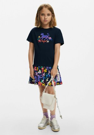 Mörkblå t-shirt med livlig blommöster och tigerdesign, ihopparad med en färgglad mönstrad kjol. Silverfärgade sneakers och en liten vit handväska fulländar looken.