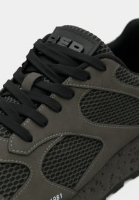 Sport shoe with a gray mesh upper, black laces, and textured sole. Features subtle branding and a perforated design for breathability.