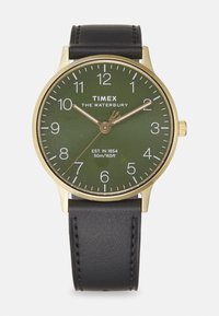 Złoty zegarek Timex z zieloną tarczą, czarnym skórzanym paskiem i białymi znacznikami godzin. Posiada funkcję datownika i jest wodoodporny do 50 m.
