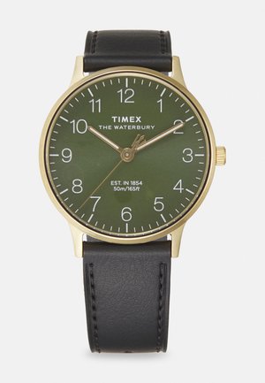 Kuldtooniline Timex kell rohelise kellapinnaga, musta nahkrihmaga ja valgete tunnimarkeritega. Omab kuupäevafunktsiooni ja on veekindel kuni 50m.