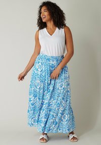 Weißes ärmelloses Oberteil kombiniert mit einem blau-weißen gemusterten Maxikleid mit gestuften Design und elastischem Bund. Tragen mit weißen Sandalen.