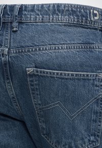 Πίσω όψη μπλε τζιν τζινών που δείχνει τη μέση, θηλιά ζώνης και μια πίσω τσέπη με διπλή ραφή σε σχήμα V.