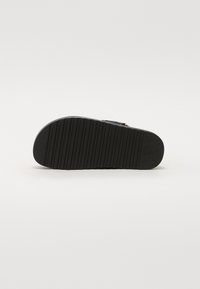 Black sandal with a textured rubber sole, featuring a slip-resistant bottom, adjustable strap, and understated hardware accent.