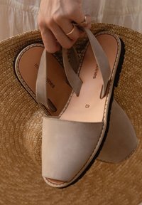 Sandales beiges à enfiler avec un dessus en cuir lisse, à bout ouvert, et semelle plate en caoutchouc noir, posées sur un chapeau de paille. Taille 40.