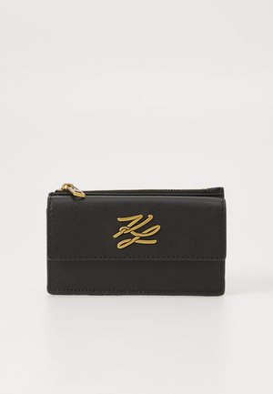 Μαύρο δερμάτινο πορτοφόλι με χρυσό λογότυπο στο μπρος μέρος. Διαθέτει κλείσιμο με φερμουάρ και αντίθεση ραφής για πρόσθετη λεπτομέρεια.
