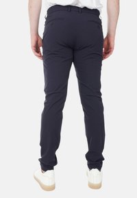 Pantaloni blu navy con un design aderente, realizzati in tessuto liscio, con due tasche posteriori e passante per cintura. Indossati con sneaker bianche.
