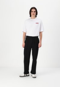 White t-shirt with red text, black sweatpants with drawstring waist, and white sneakers with black accents; minimalistic and fitted design.